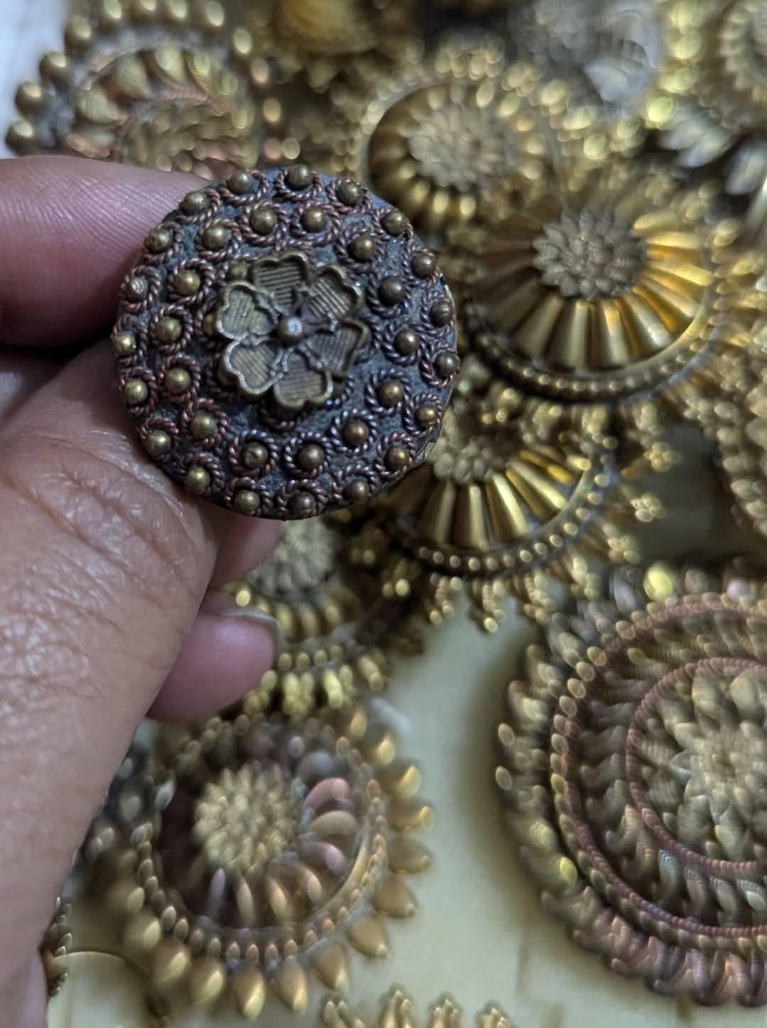 Hand holding an intricately designed antique-style brass button with floral patterns.